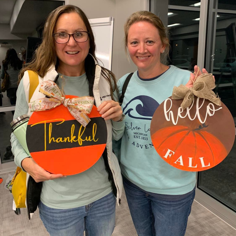two women holding round thankful signs
