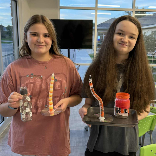 Two teens holding candles and candleholders they made